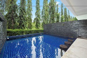 Una piscina con piso de baldosas, rodeada por un muro de piedra y abundante vegetación.