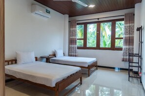 Ein Zimmer mit zwei Holzbett, einem kleinen Tisch, einer Klimaanlage und einem Fenster mit Vorhängen.
