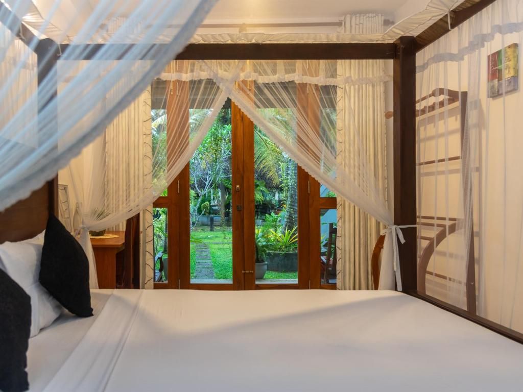 Een slaapkamer met een groot bed, een hemelbed en uitzicht op een tuin door glazen deuren.