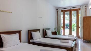 A hotel room with two single beds, a wooden wardrobe, and a sliding glass door leading to a balcony.
