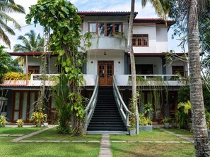 Ein zweistöckiges Haus mit einer zentralen Treppe, umgeben von üppiger Vegetation und Palmen.