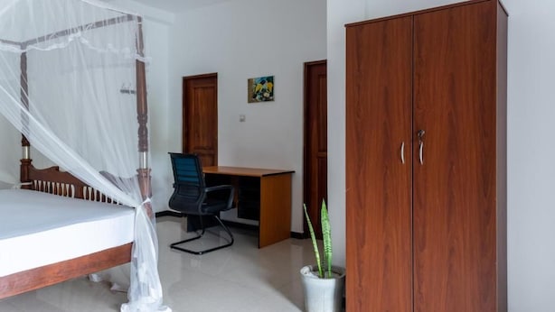 Un dormitorio con cama, escritorio, silla, armario y planta en maceta.