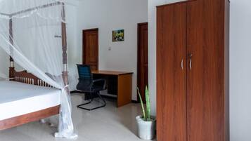 A bedroom with a bed, a desk, a chair, a wardrobe, and a potted plant.