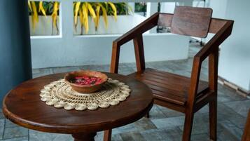 A round wooden table with a woven placemat and a bowl of fruit. A wooden chair is positioned behind the table.