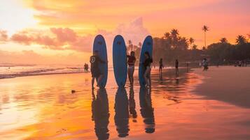 A beach scene with surfers holding surfboards, palm trees, and a sunset.