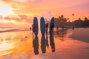 Eine Strandansicht mit Surfern, die Surfbretter halten, Palmen und einem Sonnenuntergang.