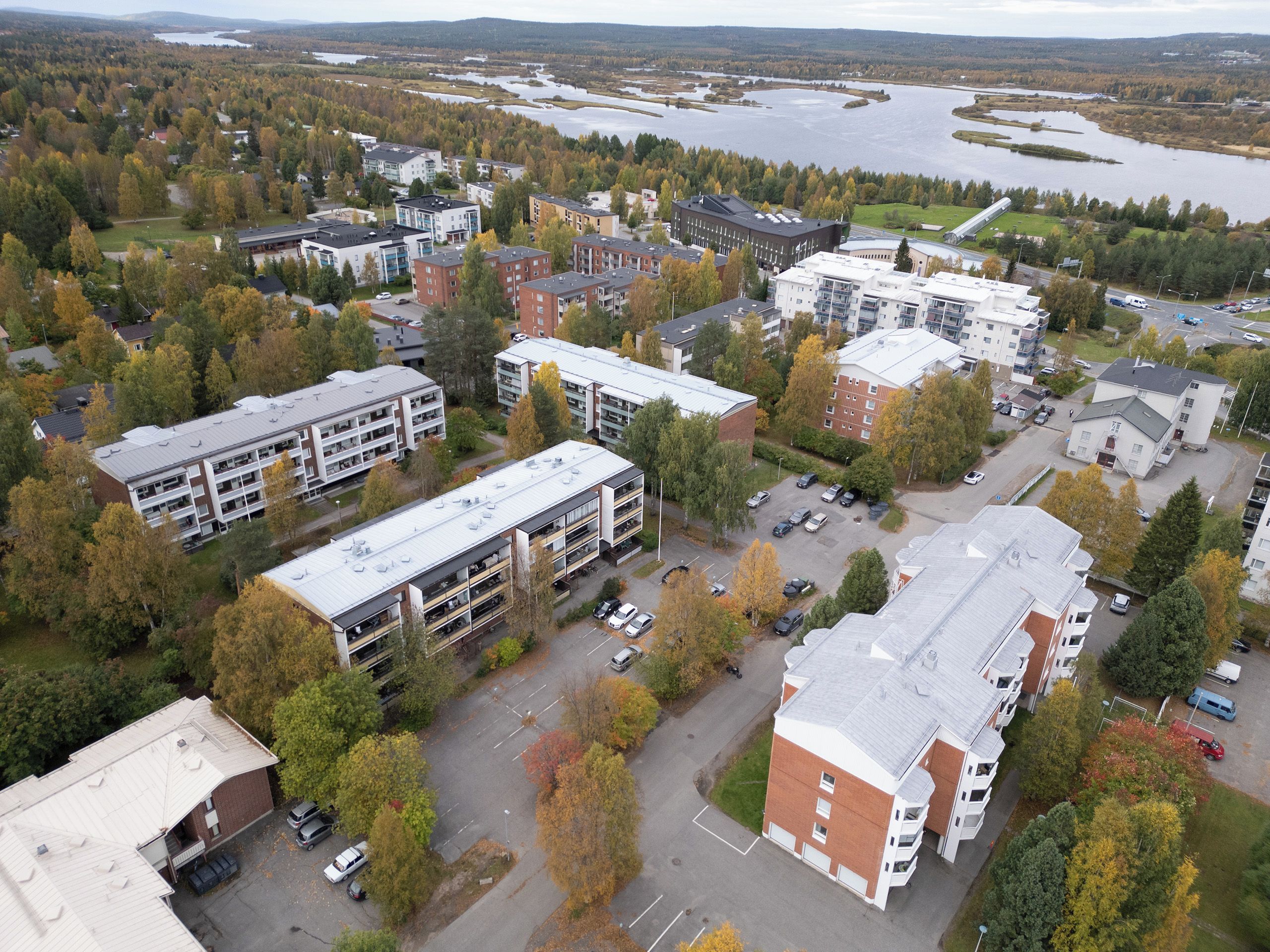 An aerial view of a residential area with multiple buildings, a parking lot, and a river in the background.