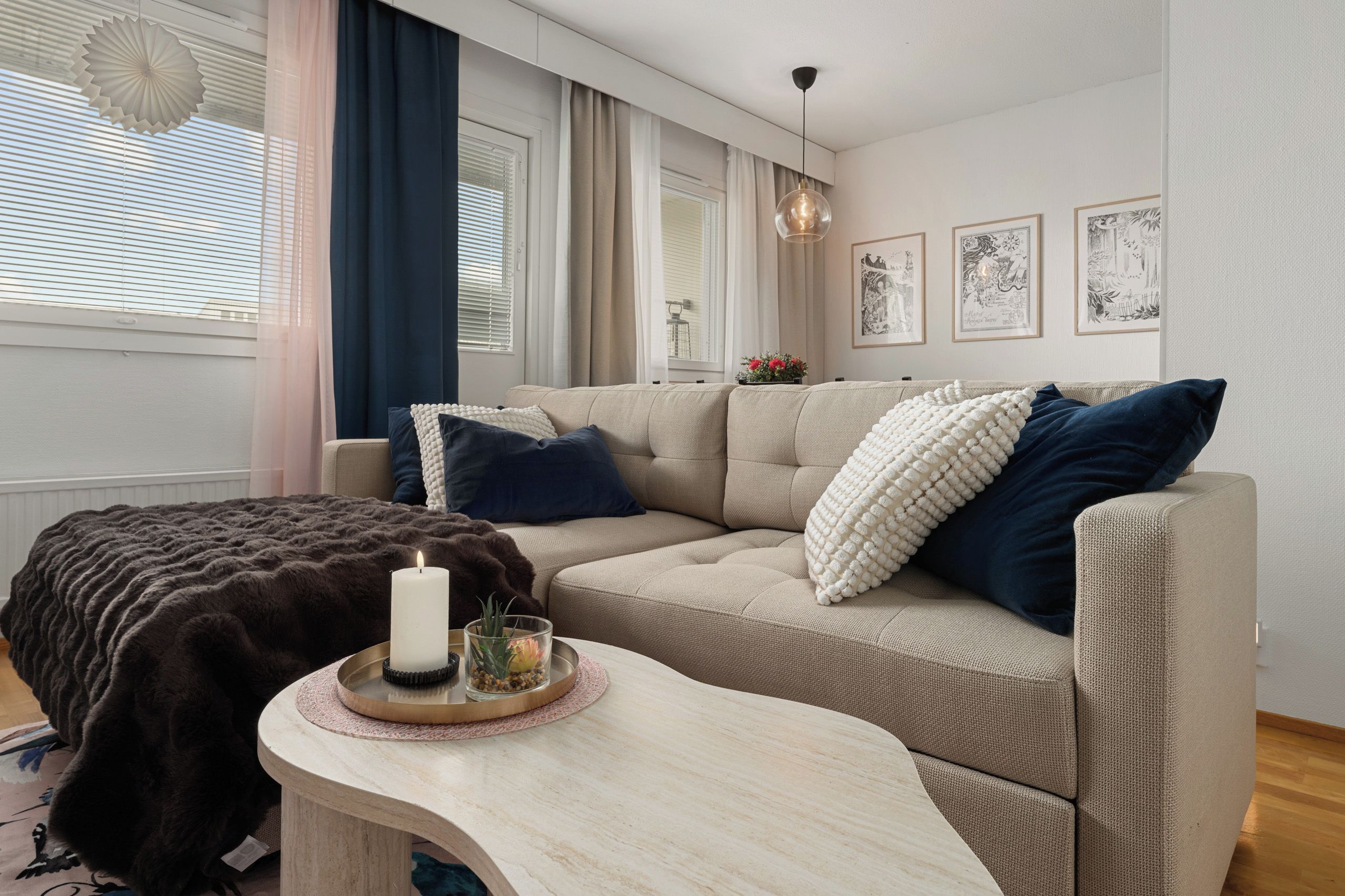 A modern living room with a beige sofa, a round coffee table, and a dark throw blanket.