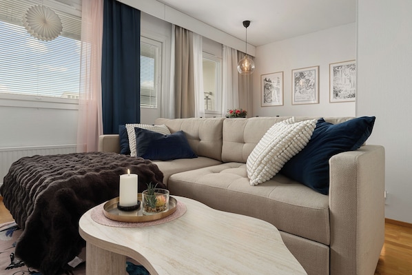 Un salon moderne avec un canapé beige, une table basse ronde et un plaid foncé.