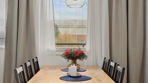 Ein Essbereich mit einem Holztisch, Stühlen, einer Vase mit roten Blumen und einem Fenster mit Jalousien.