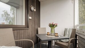 Ein kleiner Sitzbereich im Freien mit Korbstühlen, einem Tisch, einer Topfpflanze und einem Fenster mit Jalousien.