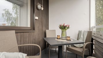 A small outdoor seating area with wicker chairs and a table, a potted plant, and a window with blinds.