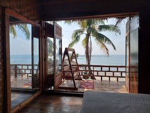 A room with a large sliding glass door leading to a beach with a swing chair and a view of the ocean.