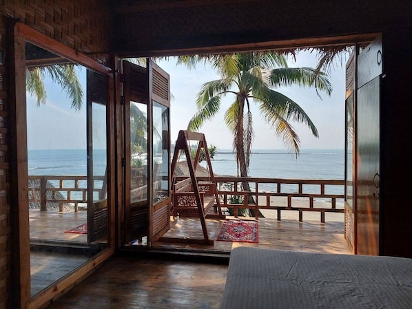 A room with a large sliding glass door leading to a beach with a swing chair and a view of the ocean.
