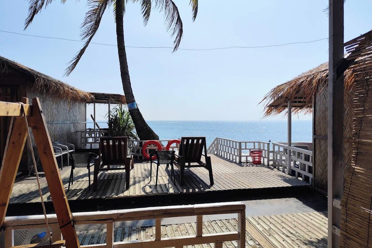 A wooden deck with chairs and a table, overlooking a beach with a clear view of the ocean.