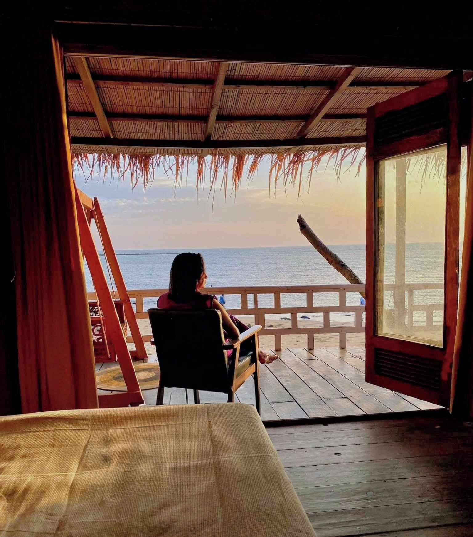 A room with a wooden deck overlooking a body of water, a bed, and a window with a view of the sea.