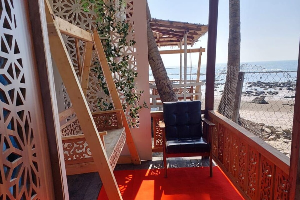 A covered outdoor seating area with a red carpet, wooden furniture, and a view of the beach.