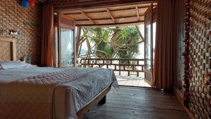 A room with a bed, a wooden floor, a balcony with a view of palm trees, and a woven wall decoration. - Sailor Eco Resort. Saint Martin (Chittagong Division)