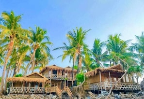 Ein Strandbungalow mit Strohdach, umgeben von Palmen.