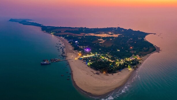 An aerial view of a coastal area with a beach, a dock, and a cluster of lights indicating a populated area. - Sailor Eco Resort. Saint Martin (Chittagong Division)
