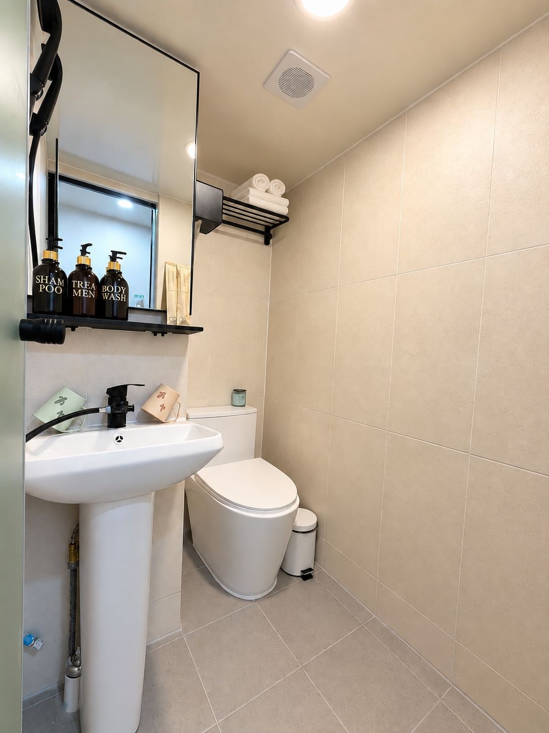 Un baño con lavamanos blanco, inodoro y repisas con artículos de aseo.