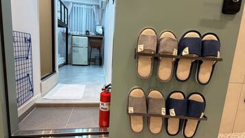 Een gang met een brandblusser, een schoenenrek met slippers en een kijkje naar een keuken.