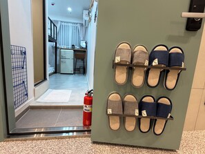 A hallway with a fire extinguisher, a shoe rack with slippers, and a glimpse of a kitchen area.