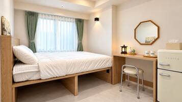 A compact room with a bed, desk, chair, and a small refrigerator.
