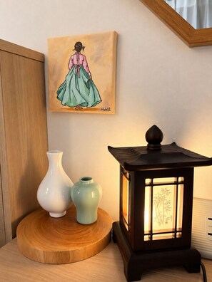 A wooden cabinet, a painting of a woman in a dress, two vases, and a lit lantern on a wooden table.