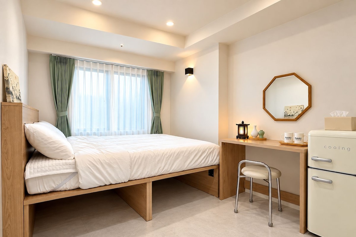 A compact room with a bed, desk, chair, and a small refrigerator.
