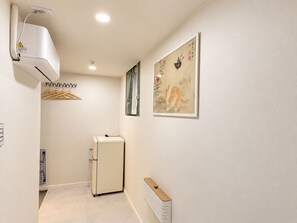Una habitación con aire acondicionado blanco, un refrigerador pequeño, un radiador y un cuadro en la pared.