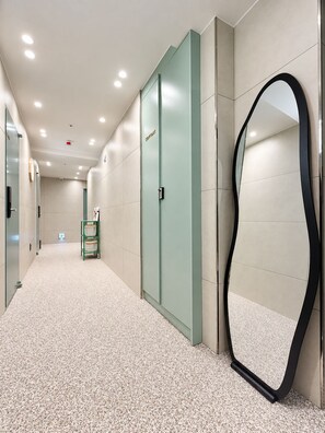 A hallway with a green elevator, a mirror, and a green storage cart.