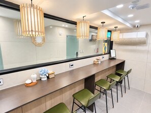 A modern kitchen with a long counter, green bar stools, pendant lights, and a large mirror.
