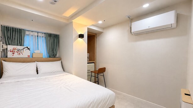 A hotel room with a bed, a desk, an air conditioning unit, and a view of a corridor. - Hub82 (Seoul)