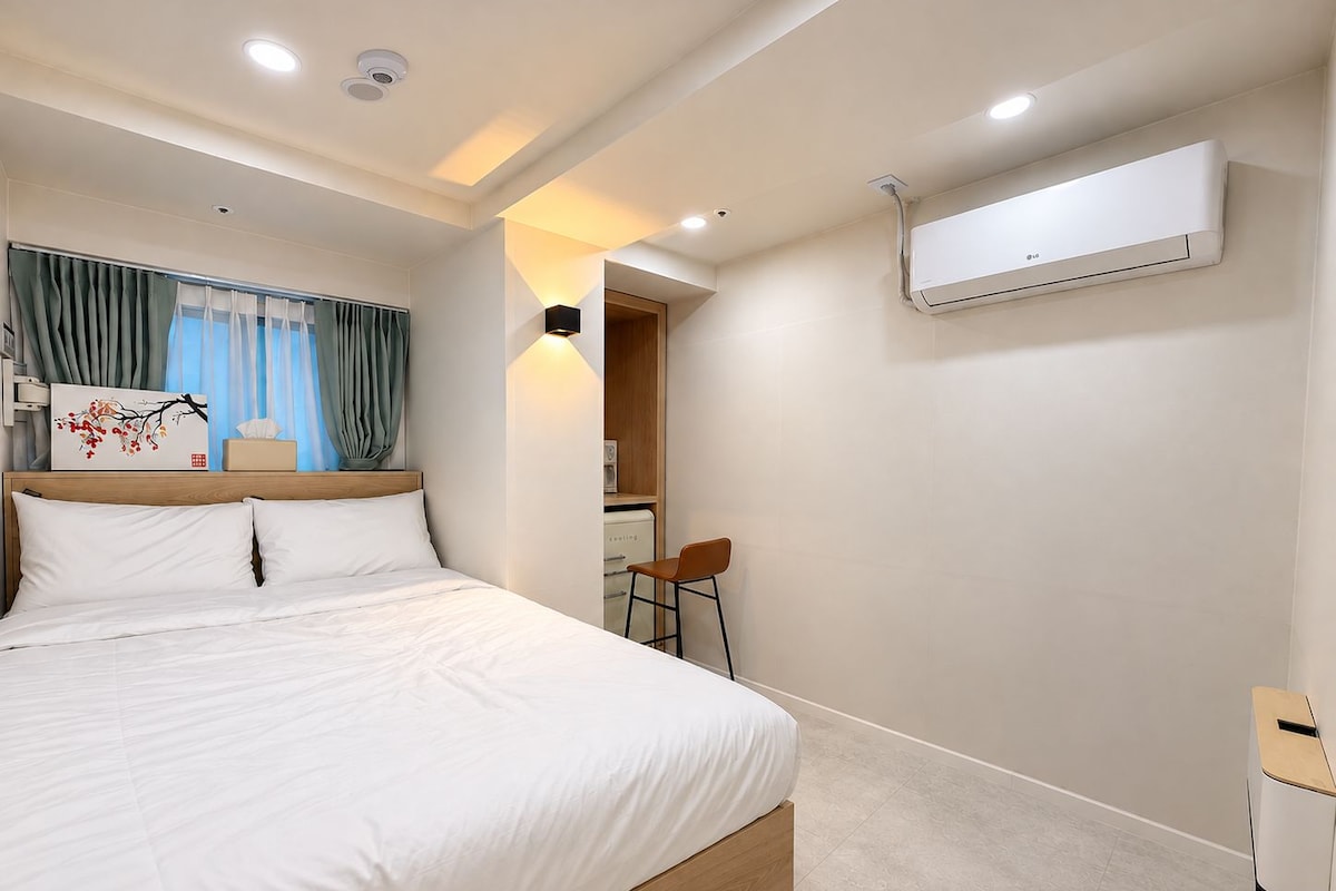 Une chambre d’hôtel avec un lit, un bureau, un appareil de climatisation et une vue sur un couloir.