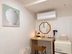 A modern room with a desk, a chair, a small refrigerator, a mirror, and a wall-mounted air conditioner.