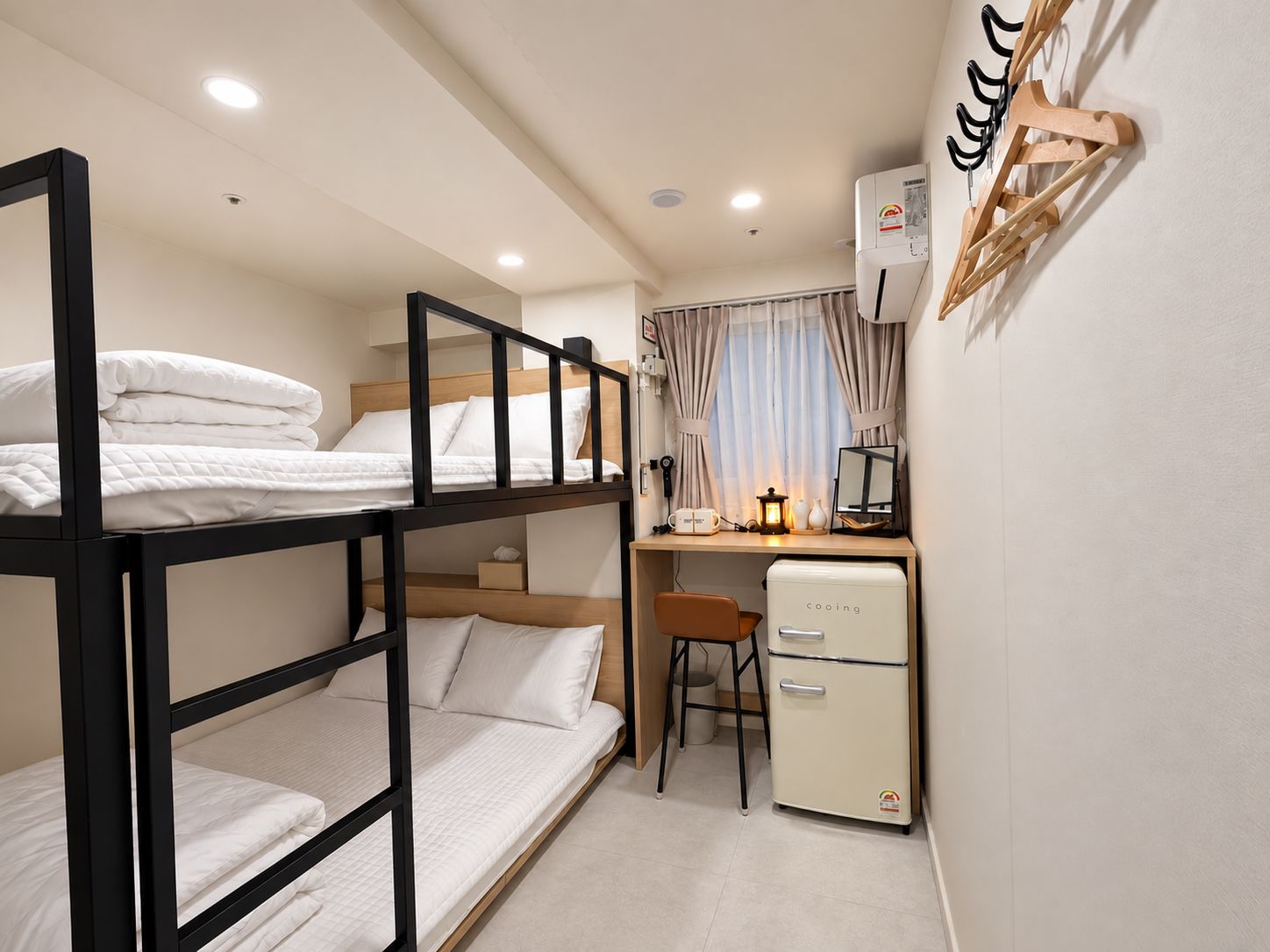 Habitación pequeña con literas, un escritorio, una silla, un refrigerador compacto y aire acondicionado instalado en la pared.