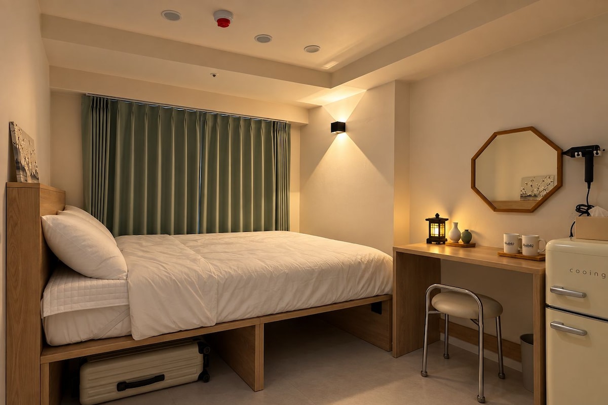 Une chambre d’hôtel de taille réduite, comprenant un lit, un bureau, une chaise et une petite kitchenette.