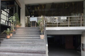A set of outdoor stairs leading to a building entrance with a metal railing, potted plants, and a sign indicating a welcome area. - Townhouse Oak Shilparamam Art (Hyderabad)