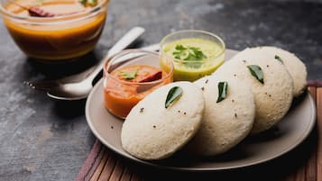 Un plato con idlis y tres chutneys diferentes, un tazón de sopa y una cuchara sobre una superficie de madera.