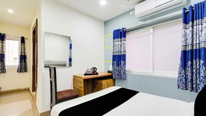 Een hotelkamer met een bed, een bureau, een stoel, een airconditioner en gordijnen.