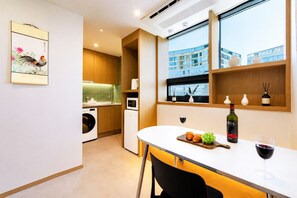 Une cuisine moderne avec un coin repas, une fenêtre donnant sur un immeuble et une bouteille de vin posée sur la table.