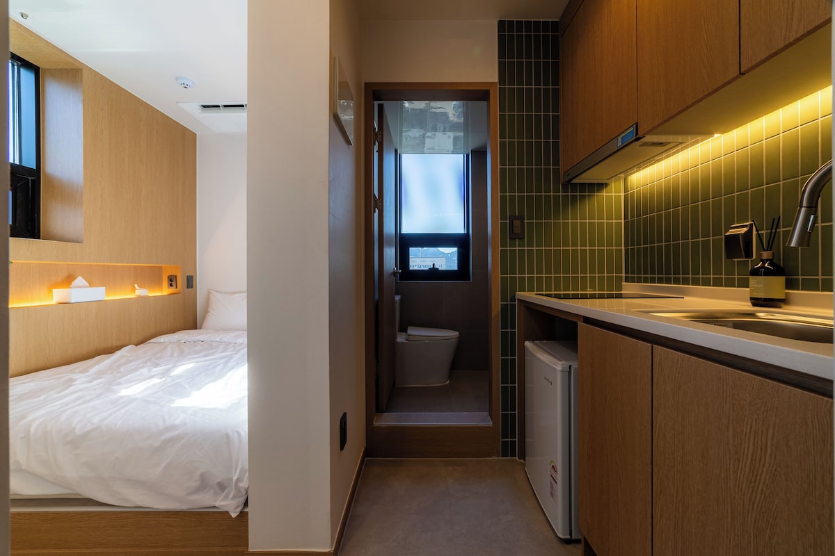 Une chambre d’hôtel de taille réduite, comprenant un lit, une petite kitchenette et une salle de bain.
