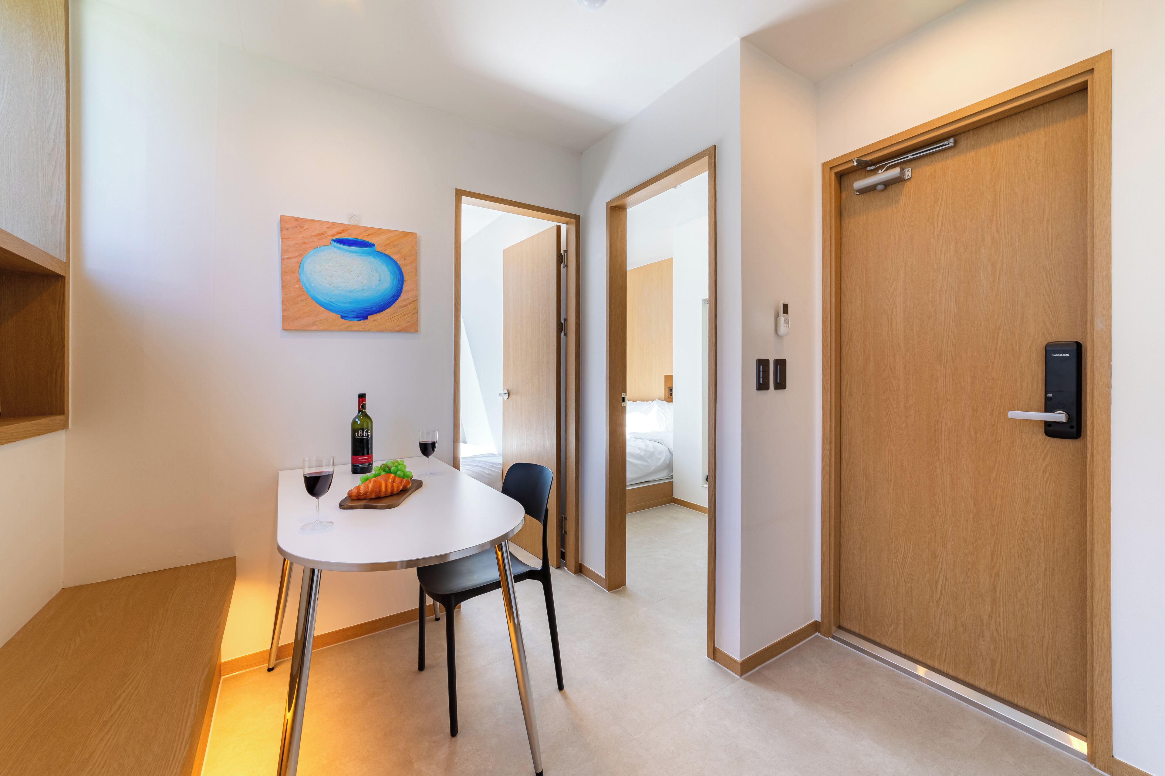 Habitación de hotel con una mesa de comedor, sillas, un cuadro, una botella de vino y un frutero.