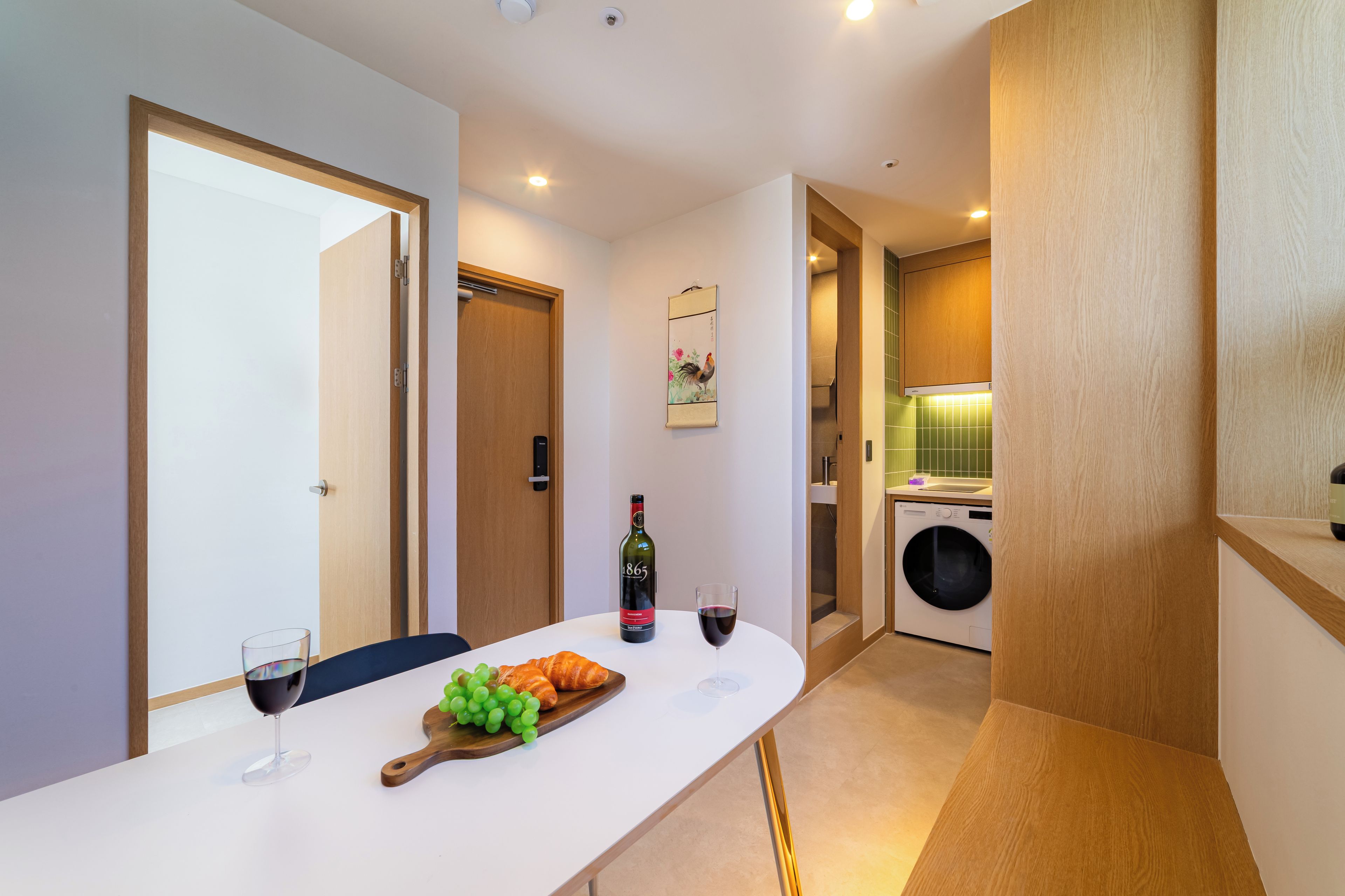 Una cocina moderna con lavadora integrada, un comedor con mesa dispuesta para dos personas, y una puerta que da a otra habitación.