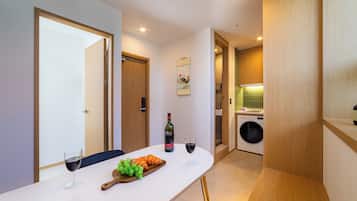 Una cocina moderna con lavadora integrada, un comedor con mesa dispuesta para dos personas, y una puerta que da a otra habitación.