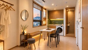 Un espacio habitable compacto con zona de comedor, lavadora y vistas a la ciudad a través de un ventanal.