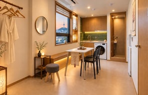 Un espace de vie compact comprenant un coin repas, un lave-linge et une vue sur le paysage urbain par une fenêtre.