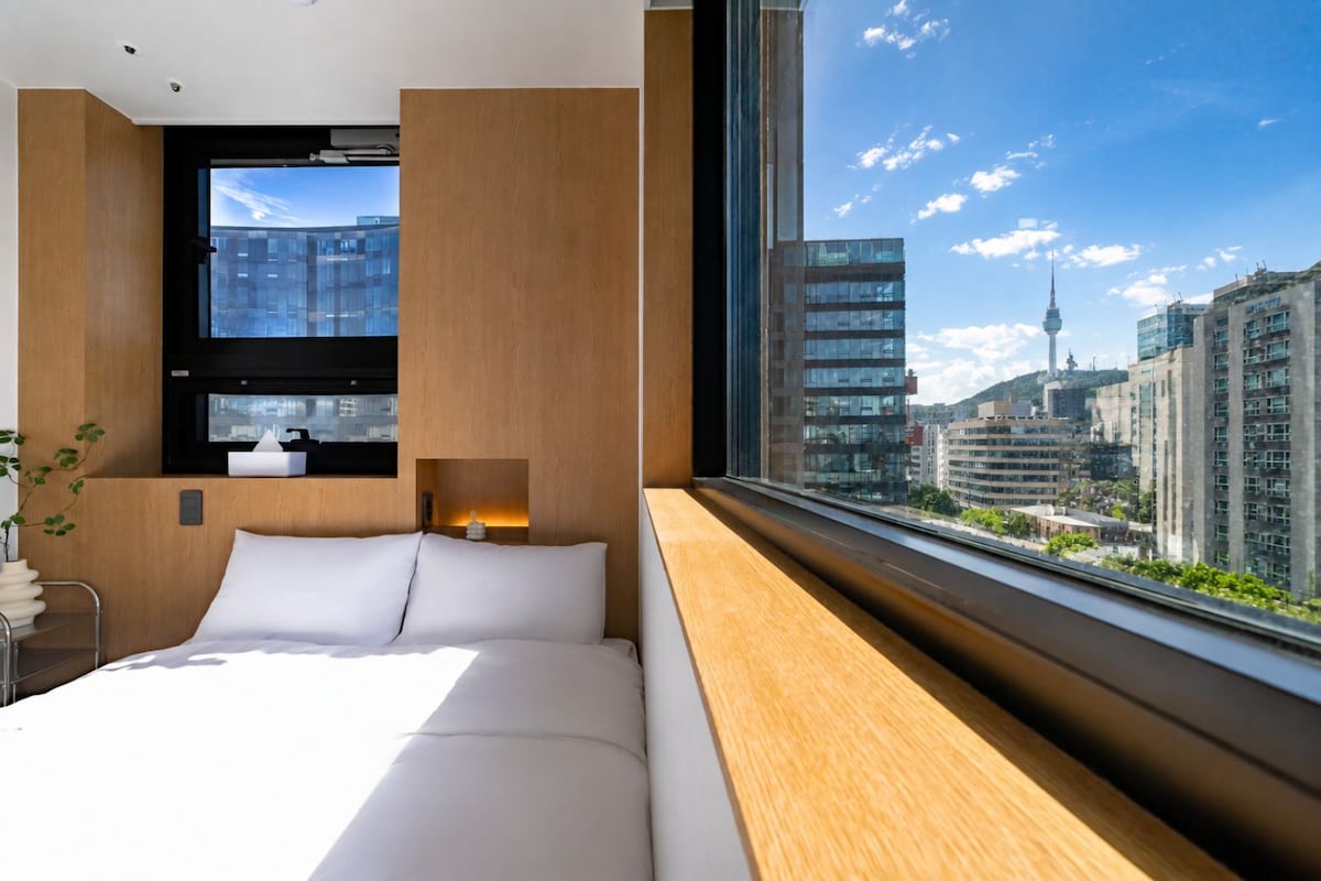 Une chambre d’hôtel moderne avec un grand lit, une table de chevet, une fenêtre donnant sur la ville et un panneau mural en bois.