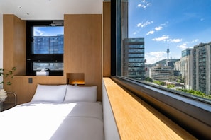 Ett modernt hotellrum med en stor säng, ett sängbord, ett fönster med utsikt över staden och en väggpanel i trä.